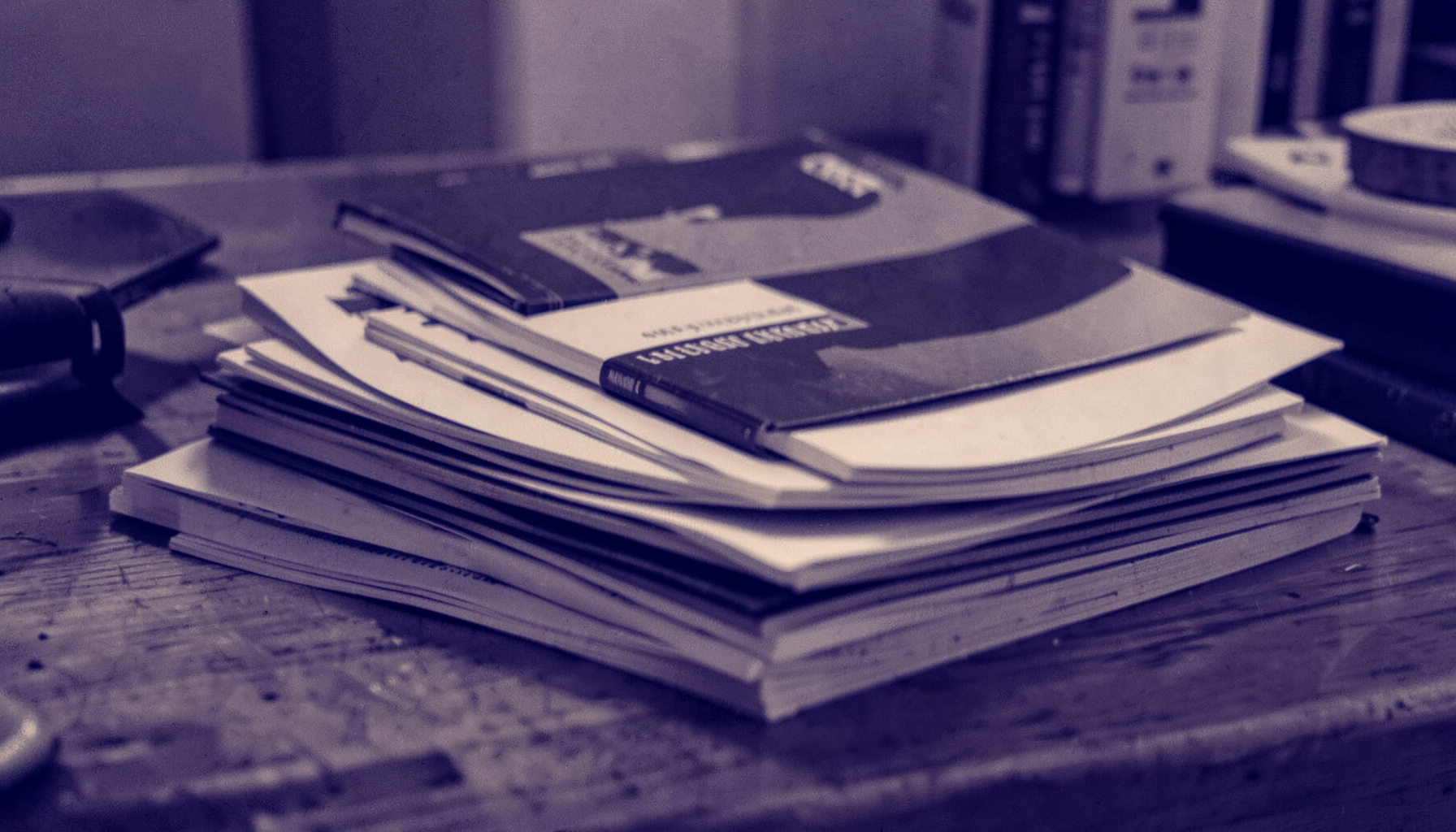 A warm duotone photograph of stacked literary journals on a wooden desk, deep navy and cream tones, quiet and contemplative mood.